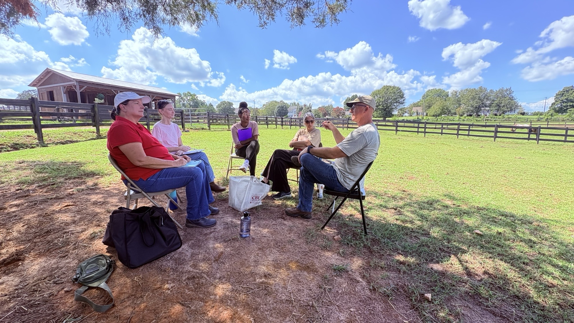 Participants and facilitators at Guiding Reins sitting in a circle chatting in the cool shade of a tree
