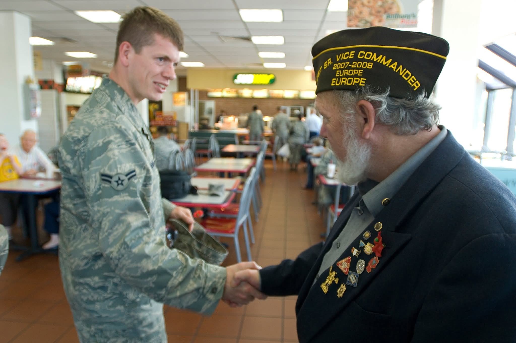 Cody Hendrick shaking hands with fellow Veteran while in uniform