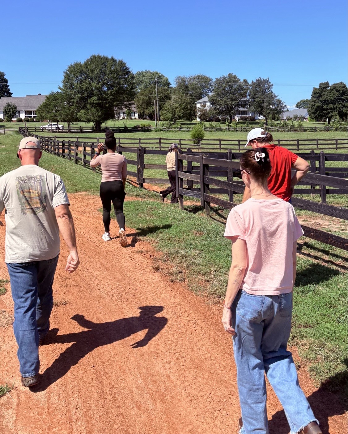 equine therapy participants walking on dirt path near the wooden fence of a pasture
