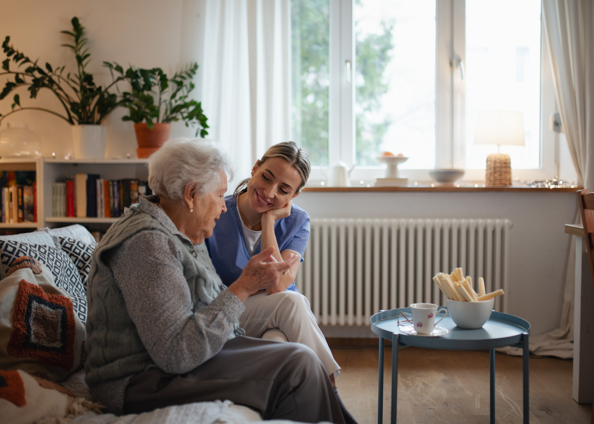 Mature adult speaking with nurse in living room on couch