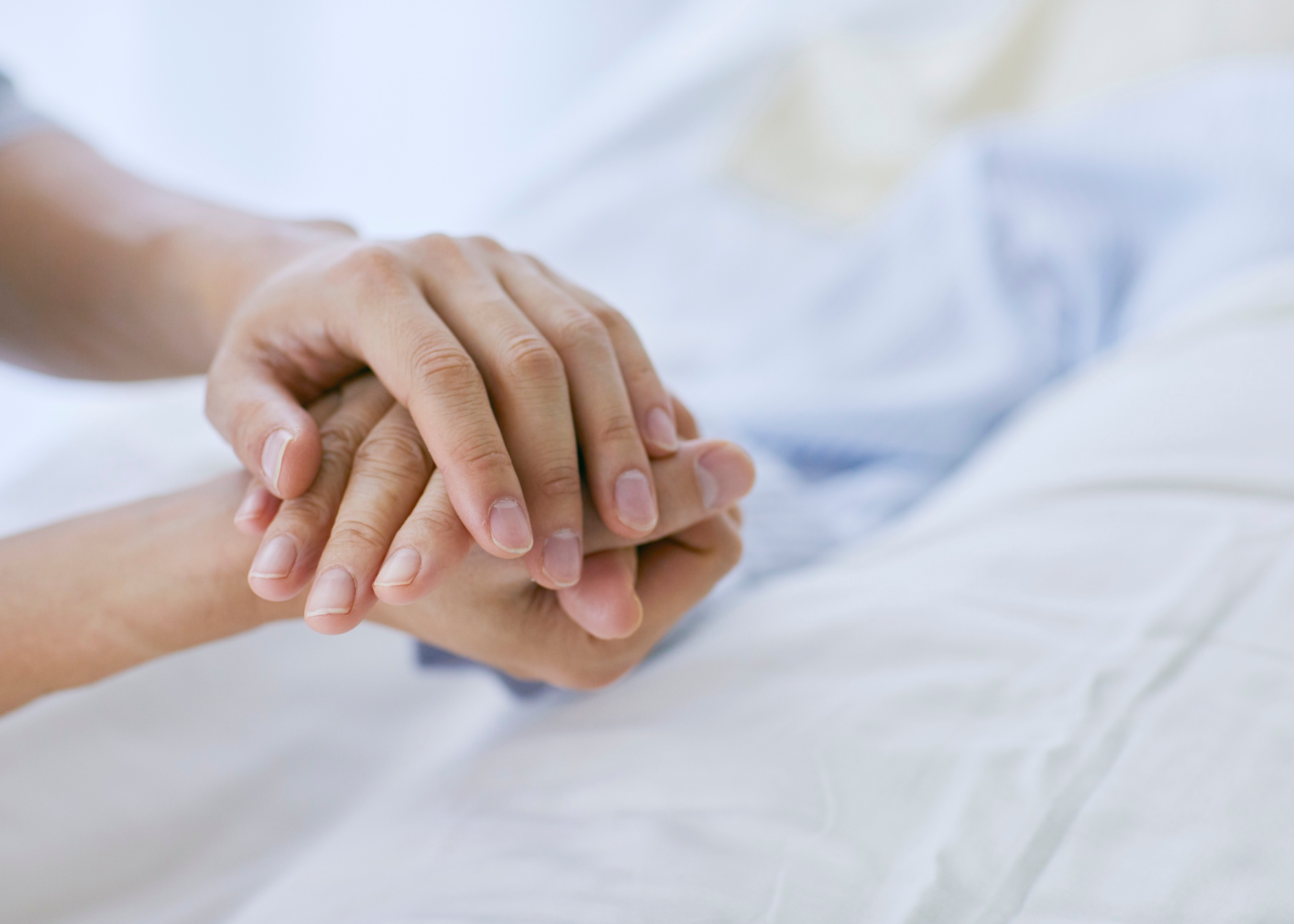 close up of two people holding hands over hospital sheets and gown